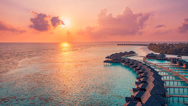 Sonnenuntergang im Meer neben Wasservillen und Holzsteg, Malediven. © Levente Bodo via Getty Images