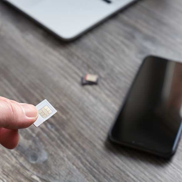 Hand mit SIM-Karte im Vordergrund, Handy auf einem Tisch im Hintergrund