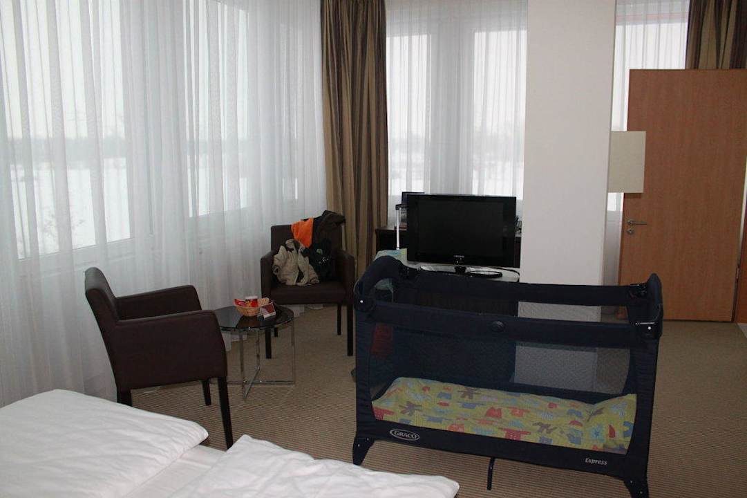 Babybett im Zimmer, daneben kleine Sitzgruppe acom Hotel München
