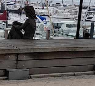 Holzfigur sitzt am Jachthafen.