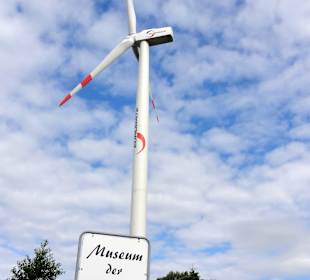 Wegweiser zum Museum vor moderner Windkraftanlage