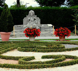 Sandfigur vor Pflanzenrabatten