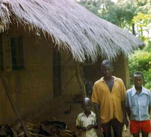 Drei Brüder vor einer typischen Savannenhütte