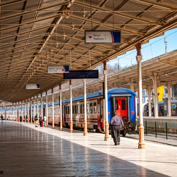 Bahnhofsgebäude mit Säulen in weißbraun mit einem bunten Zug und einem Mann