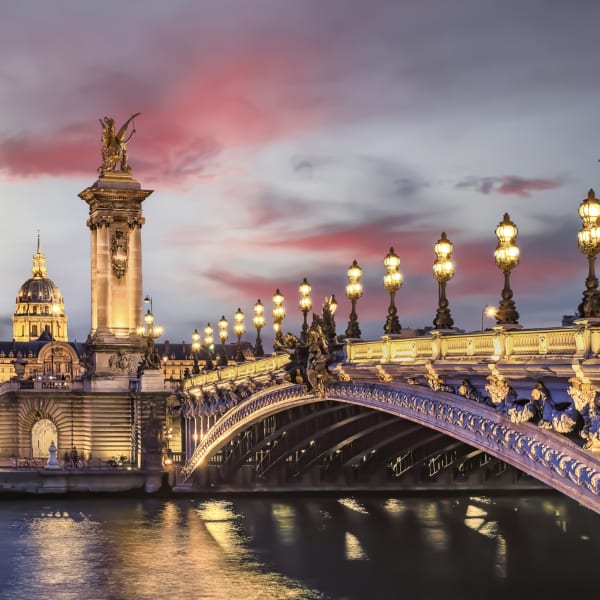 Brücke mit schöner Architektur beleuchtet von Laternen in Paris © iStock.com/StockByM