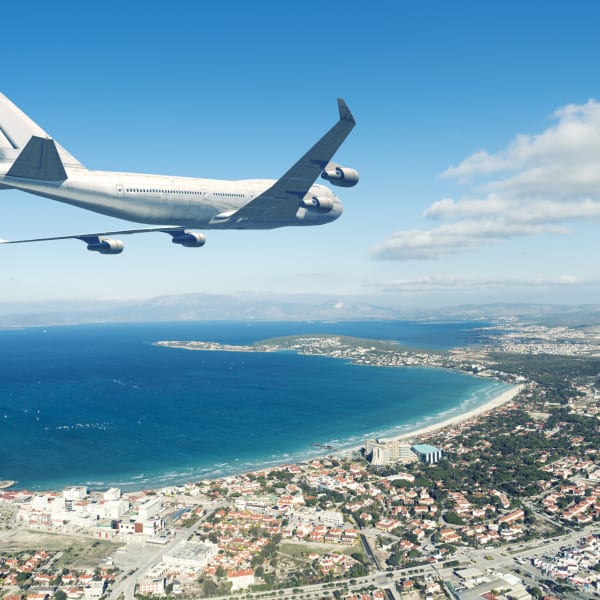 Flugzeug fliegt über eine Küstenstadt an blauem Himmel © iStock.com/jpgfactory