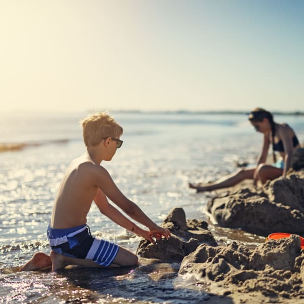 Kinder spielen am Strand und bauen eine Sandburg © iStock.com/Imgorthand