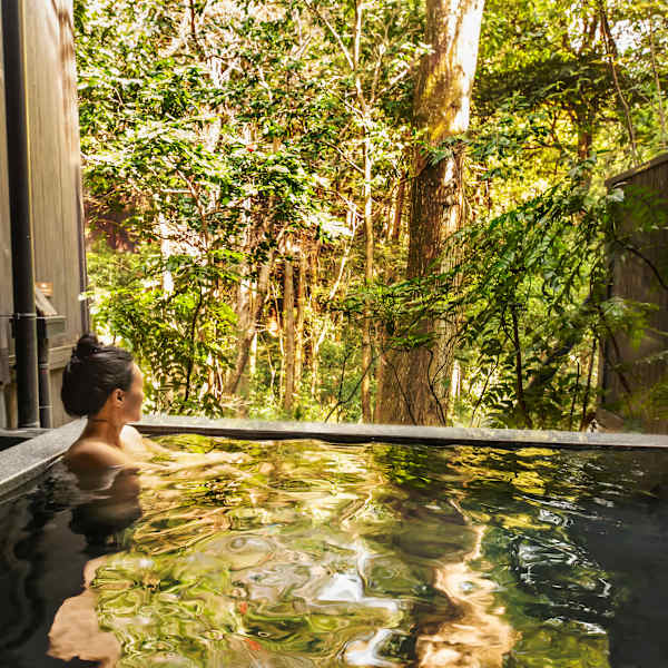 Frau baded in Onsen mit Wald im Hintergrund
