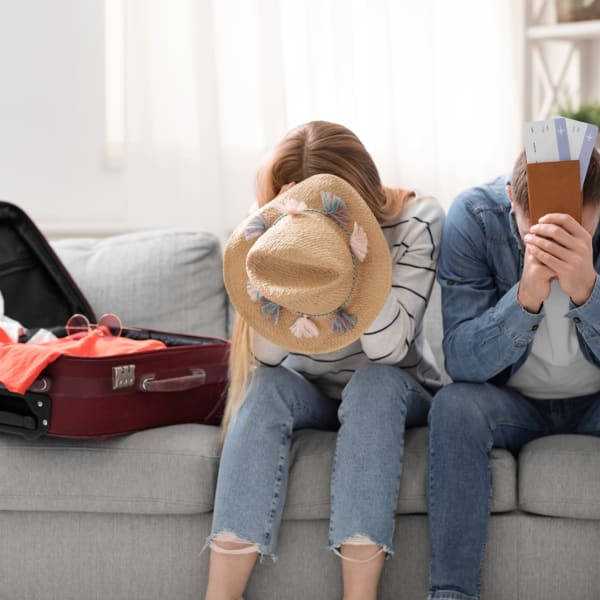 Paar sitzt traurig zu Hause in der Nähe von gepackten Koffer für den Urlaub ©iStock.com/Prostock-Studio