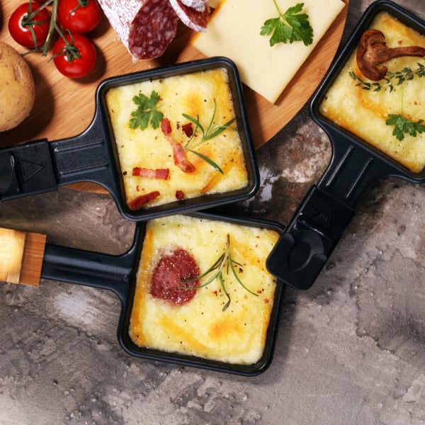 Drei kleine Pfännchen mit geschmolzenem Raclettekäse. © beats3/iStock / Getty Images Plus via Getty Images
