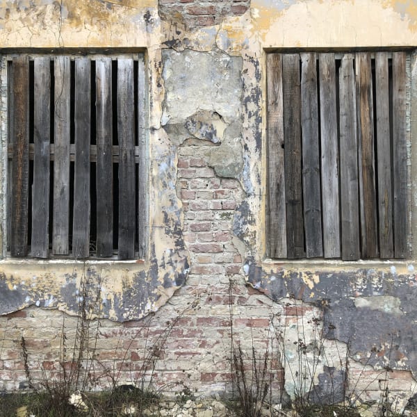 Mit Holzbrettern verschlossene Fenster eines alten Steinhauses.