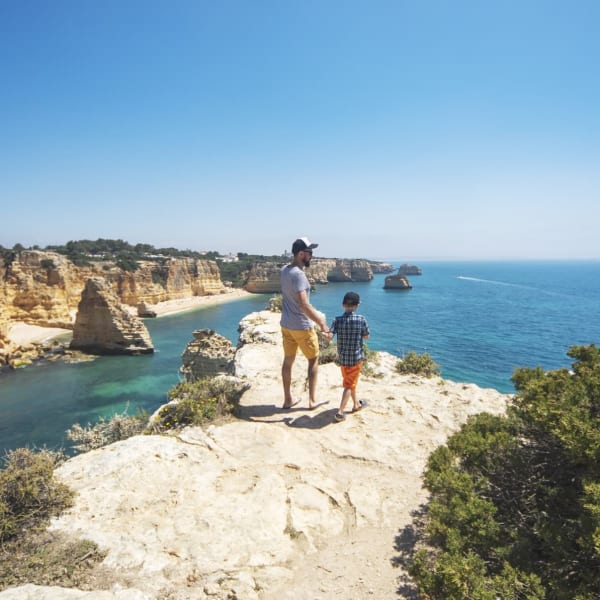 Vater und Sohn spazieren an einer Klippe entlang in der Algarve, Portugal.