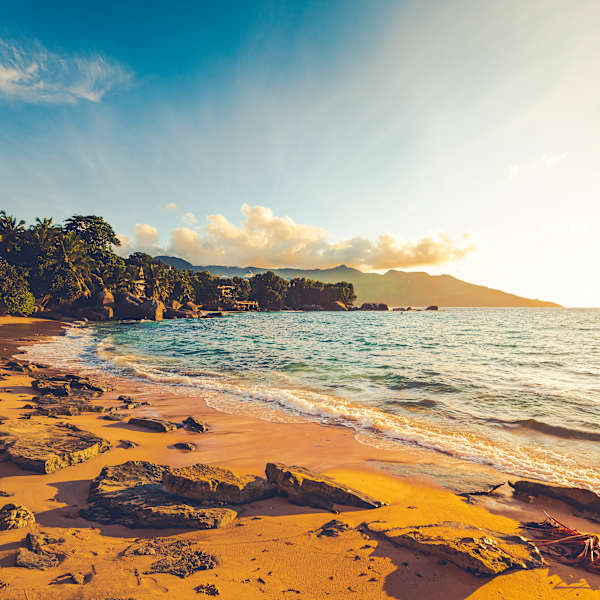 Ein Strand umgeben von Palmen mit Bergen im Hintergrund